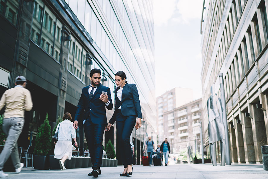 About Our Agency - Two People in Business Suits Walking Down Busy City Street
